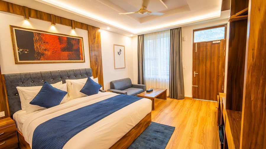 A close up shot of a room in the hotel featuring a king size bed, wooden furnishing, couch, wall paintings, and a table  | The Tattva Devprayag