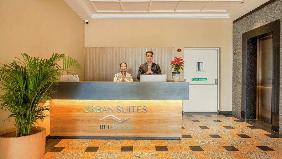 The reception at Urban Suites by BluSalzz, Jaipur, with a tiled floor, featuring seating arrangements,  plants, and two people at the desk.