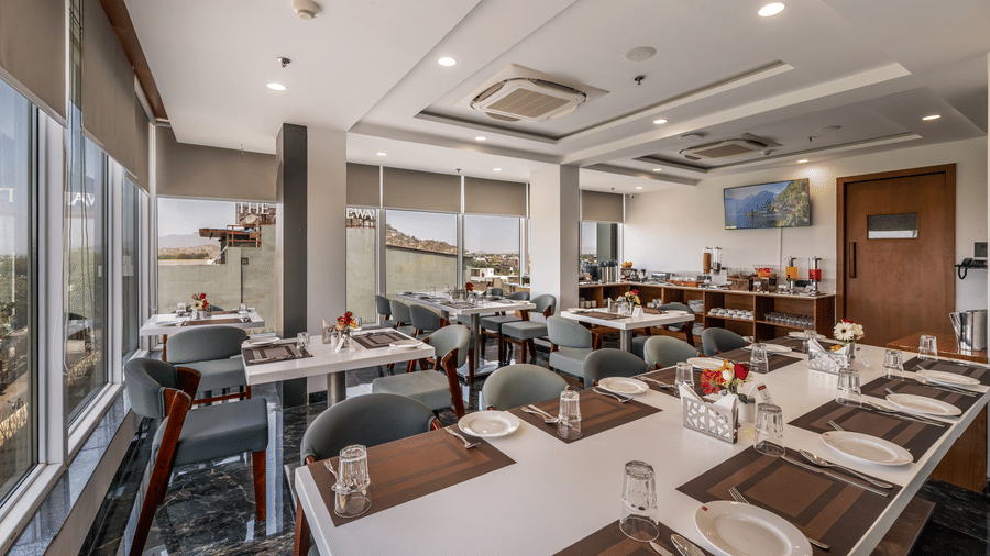 A restaurant in the best hotel in Sumerpur, Rajasthan, featuring sleek dining tables, cool chairs, and lots of windows.