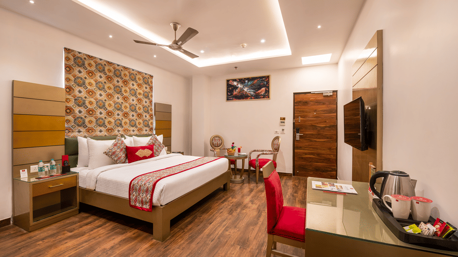 View of an Executive Room at Lords Inn Amritsar with a king bed, patterned headboard, wooden flooring, ceiling fan, and warm ambient lighting.