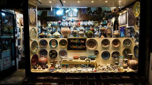 A shop window displays numerous plates, vases, and various objects arranged on shelves.