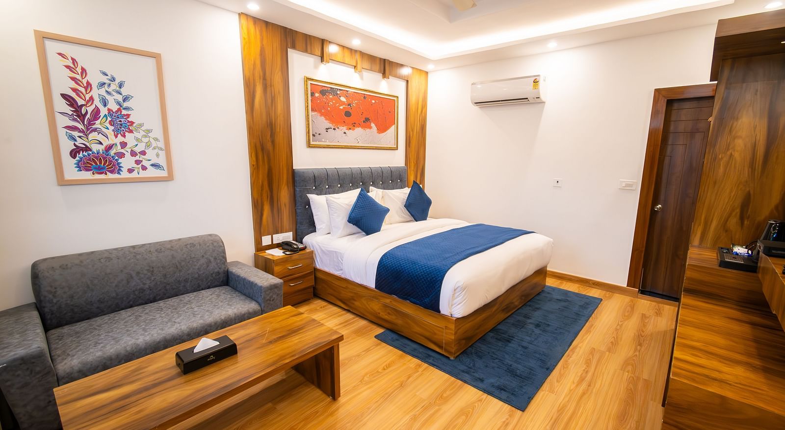 Shot of a air-conditioned room in the hotel featuring a king size bed, wooden furnishing, couch, wall paintings, and a table  | The Tattva Devprayag