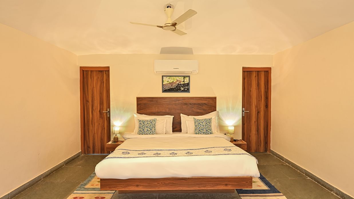 Well-lit hotel room with a double bed, minimal décor, wooden headboard, and side tables.