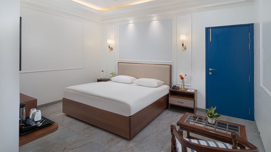 A spacious bed with bright, inviting lighting and a wooden table with a plant on it | Hotel Ganga Maiya