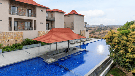 A large blue swimming pool features a swim-up bar next to multistory stone resort villas under a clear sky - Sajjan Bagh Resort and Spa, Kumbhalgarh