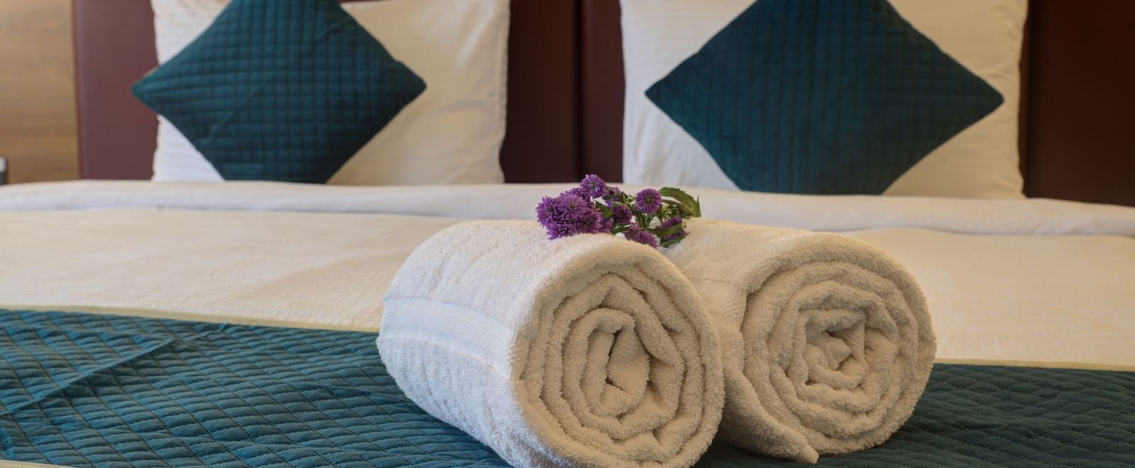 Close up shot of two white towels rolled and kept over the bed runner at Ilara Hotels & Spa, Tada.