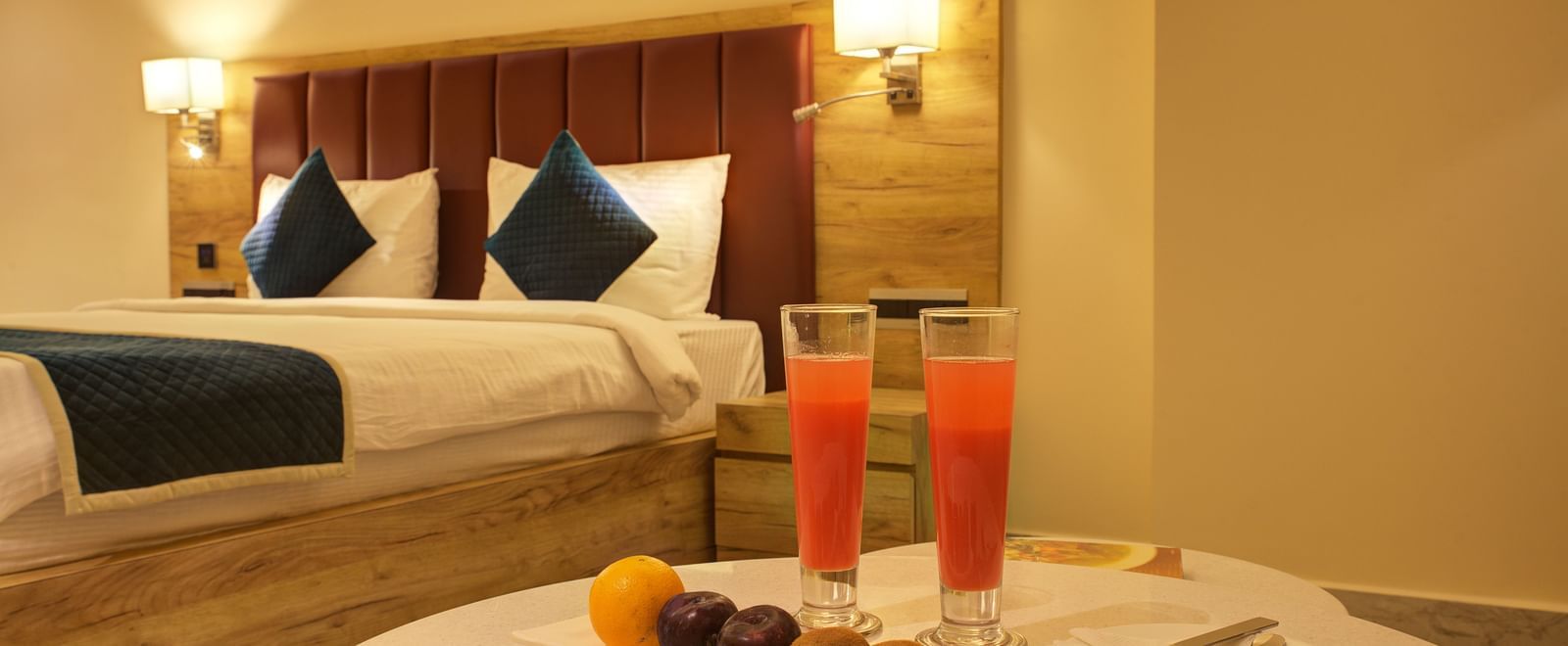A coffee table light snacks and two tall glasses of fresh juice overlooking a plush double bed at the Junior Suite at Ilara Hotels & Spa, Tada.