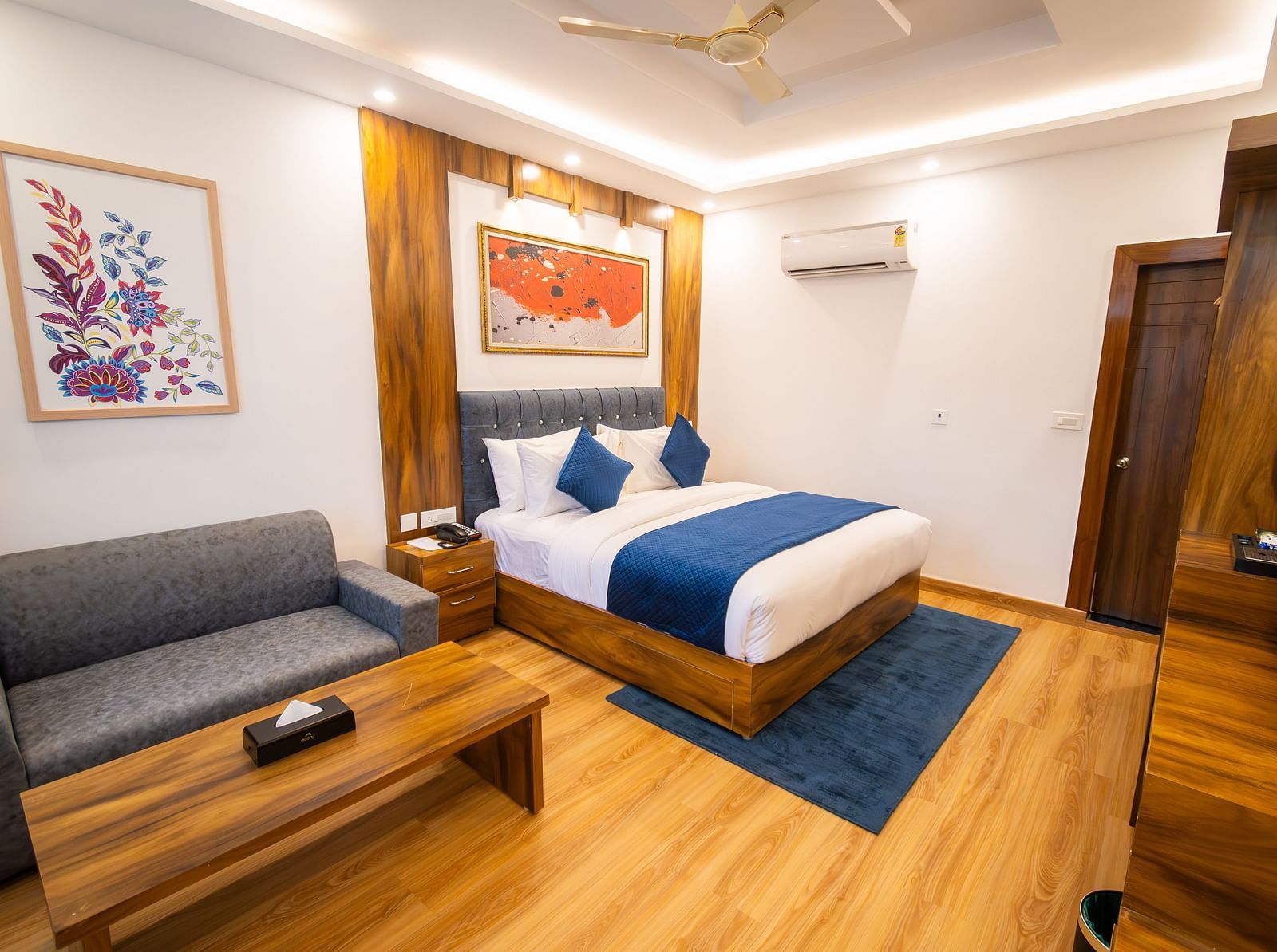 Shot of a air-conditioned room in the hotel featuring a king size bed, wooden furnishing, couch, wall paintings, and a table  | The Tattva Devprayag