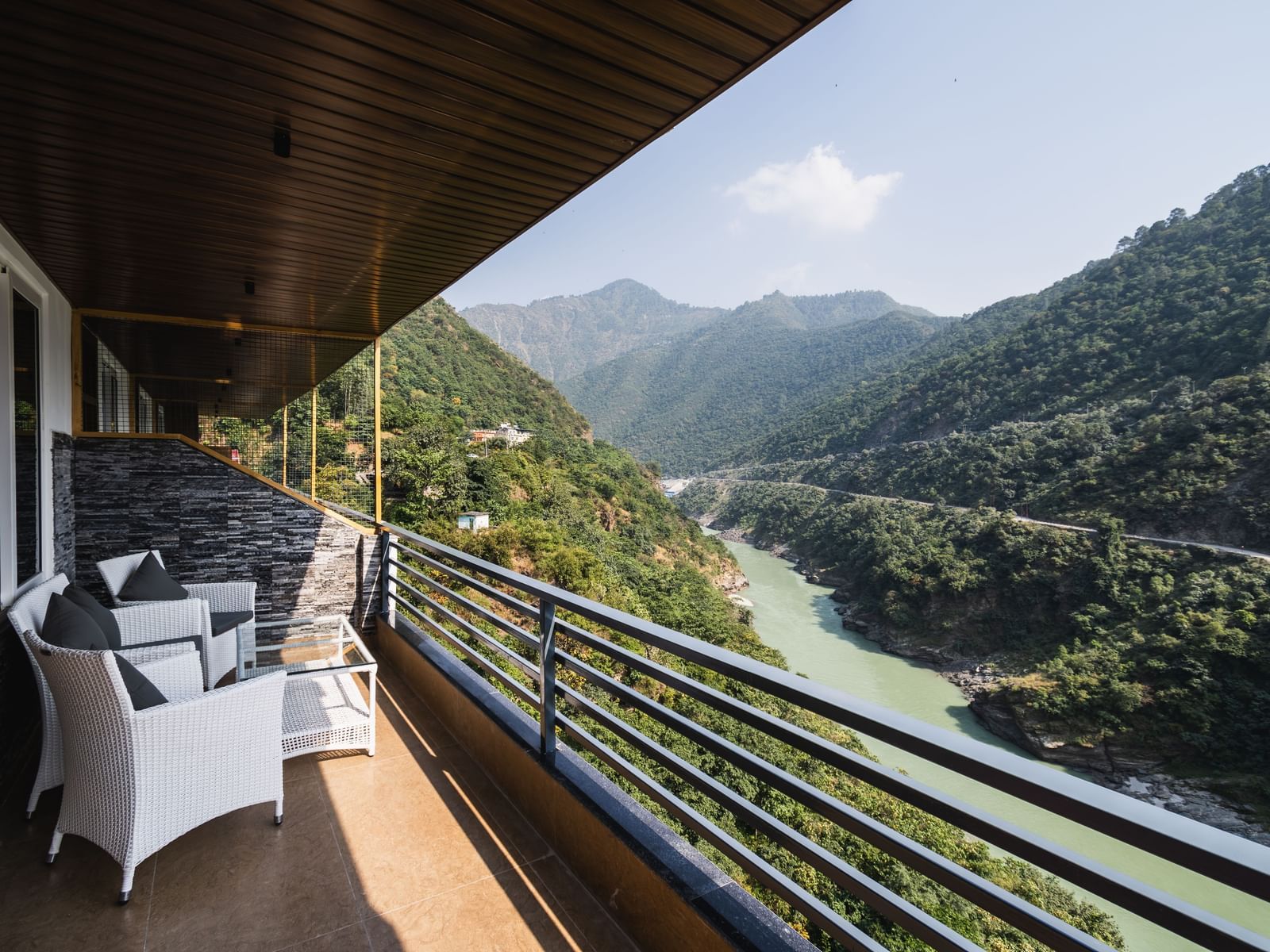 Shot of the mountains and river flowing from the balcony of the hotel featuring two white chairs and table in the morning | The Tattva Devprayag