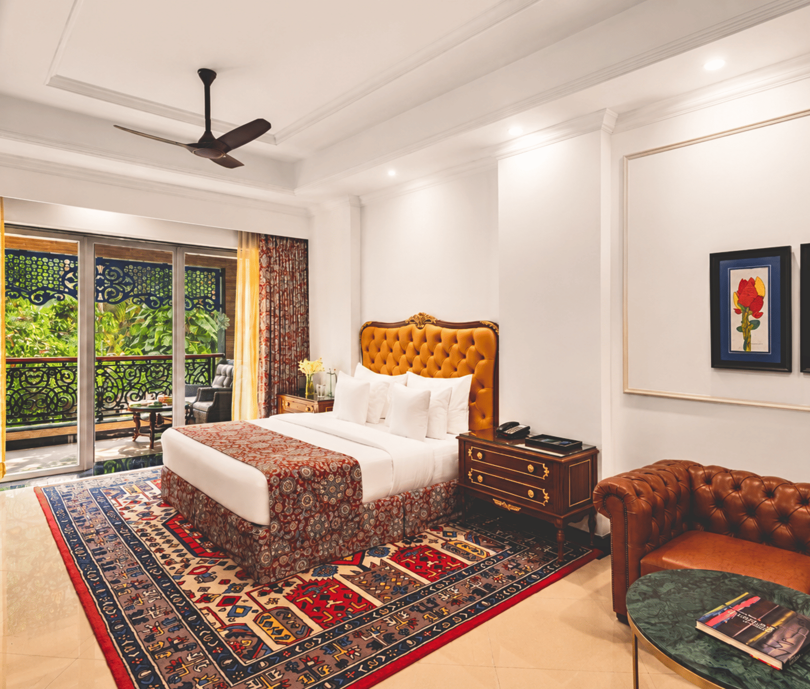King bed room with a tufted leather headboard, a sofa, floral wall art and a balcony overlooking greenery at MAYFAIR Palm Beach Resort, Gopalpur-on-Sea.