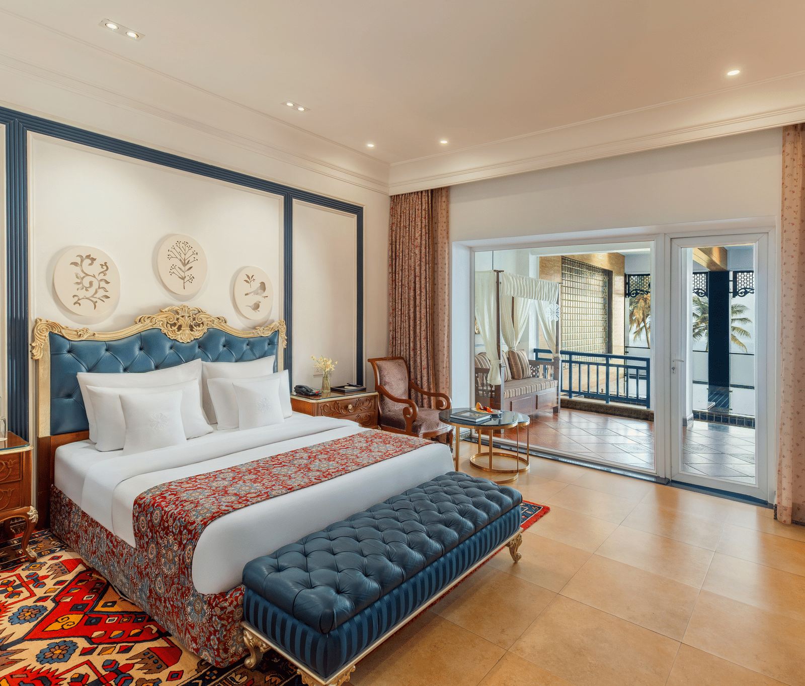 Room with a king bed, a tufted bench and sliding doors opening to a terrace with a daybed and sea beyond at MAYFAIR Palm Beach Resort, Gopalpur-on-Sea.