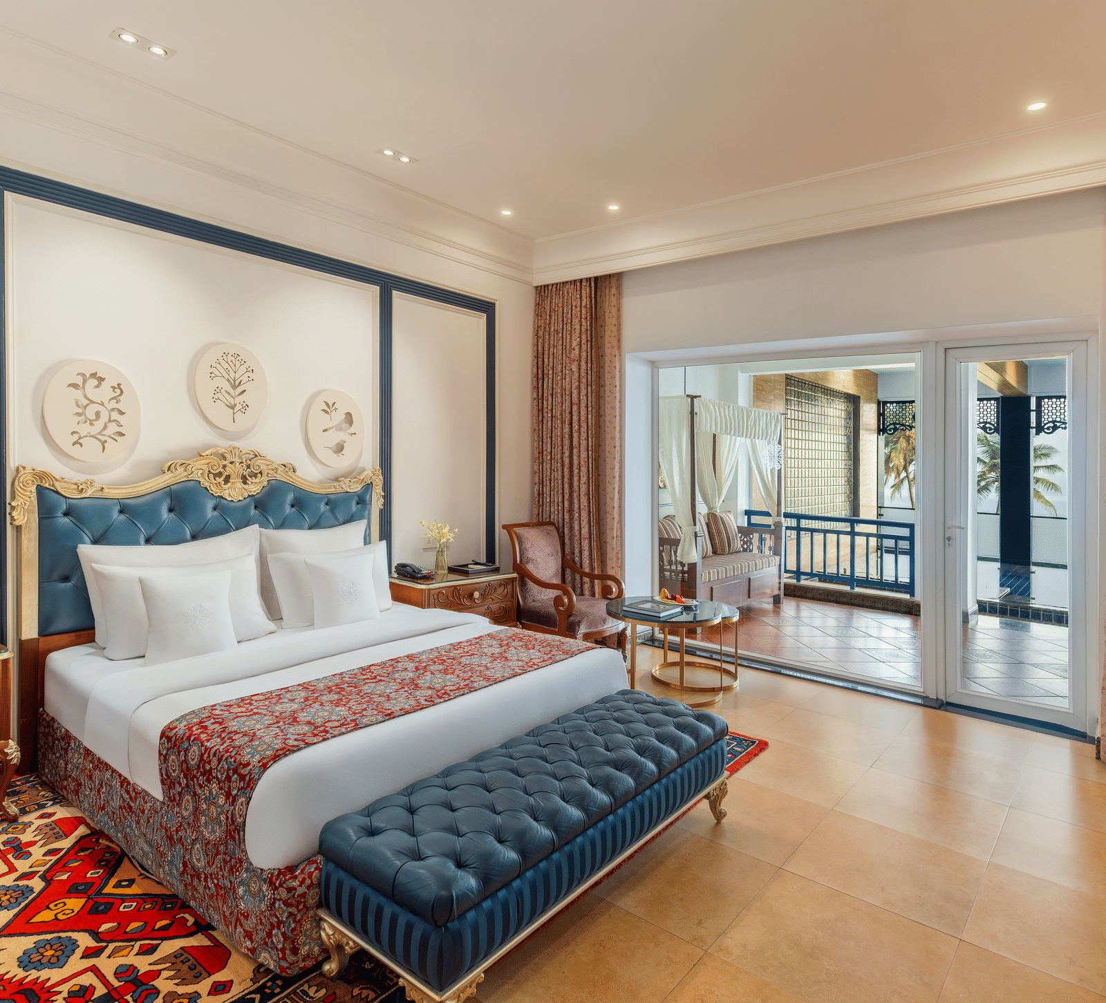 Room with a king bed, a tufted bench and sliding doors opening to a terrace with a daybed and sea beyond at MAYFAIR Palm Beach Resort, Gopalpur-on-Sea.