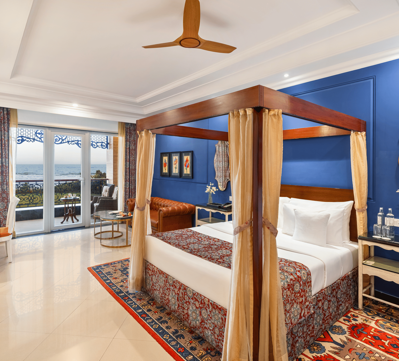 Room with a wooden four-poster bed, an armchair, a writing desk and a balcony overlooking the sea at MAYFAIR Palm Beach Resort, Gopalpur-on-Sea.