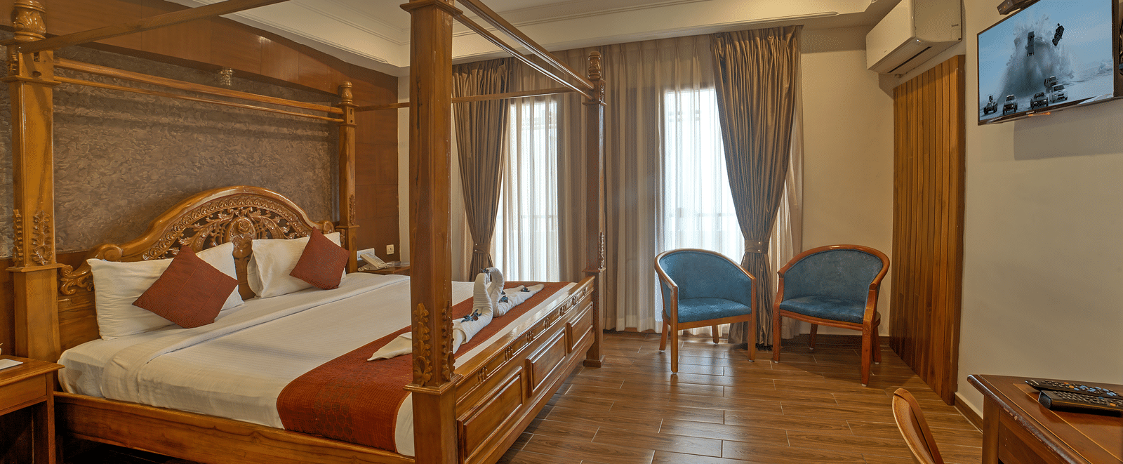 Elegant wooden bed with twin chairs and ambient lighting in a spacious room at Ilara Hotels & Spa, OMR, Chennai