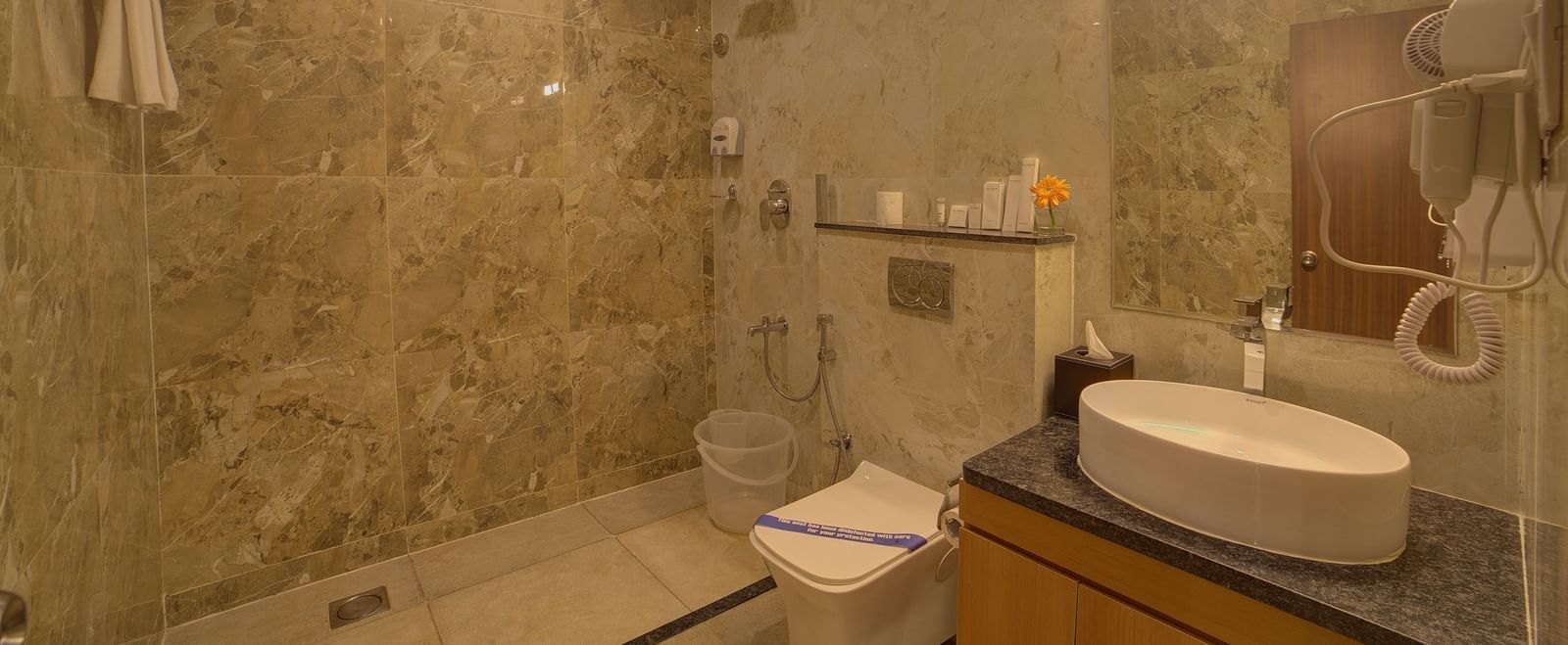 A warmly lit bathroom of the Junior Suite with a shower area along side a commode and a wash basin at Ilara Hotels & Spa, Tada.