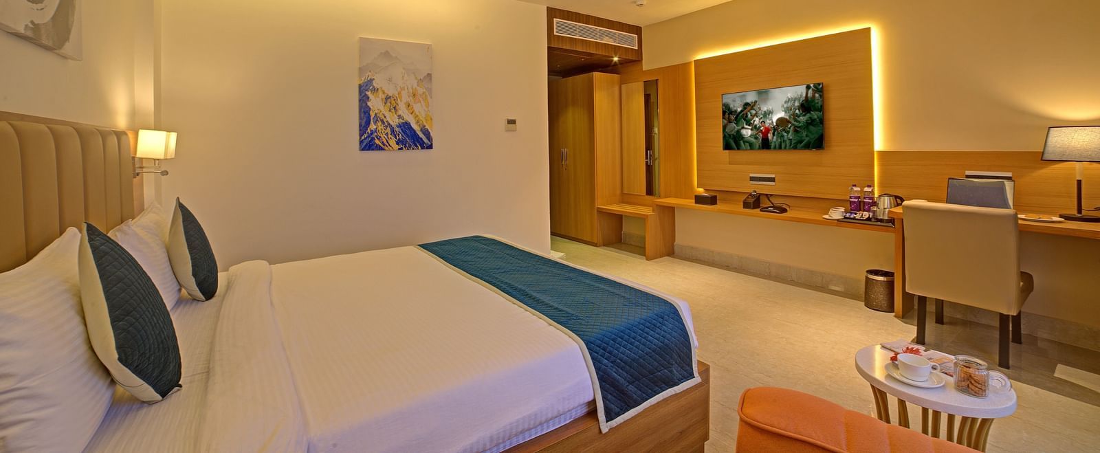 A wall mounted television in front of a comfortable double bed in front of it at in a warmly lit Signature Suite at Ilara Hotels & Spa, Tada.