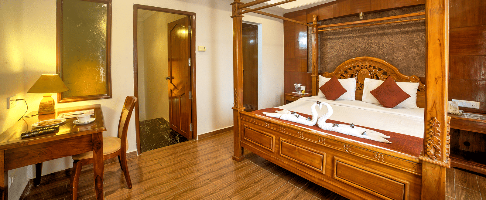 Luxurious four-poster bed with classic wooden furniture and warm ambient lighting at Ilara Hotels & Spa, OMR, Chennai