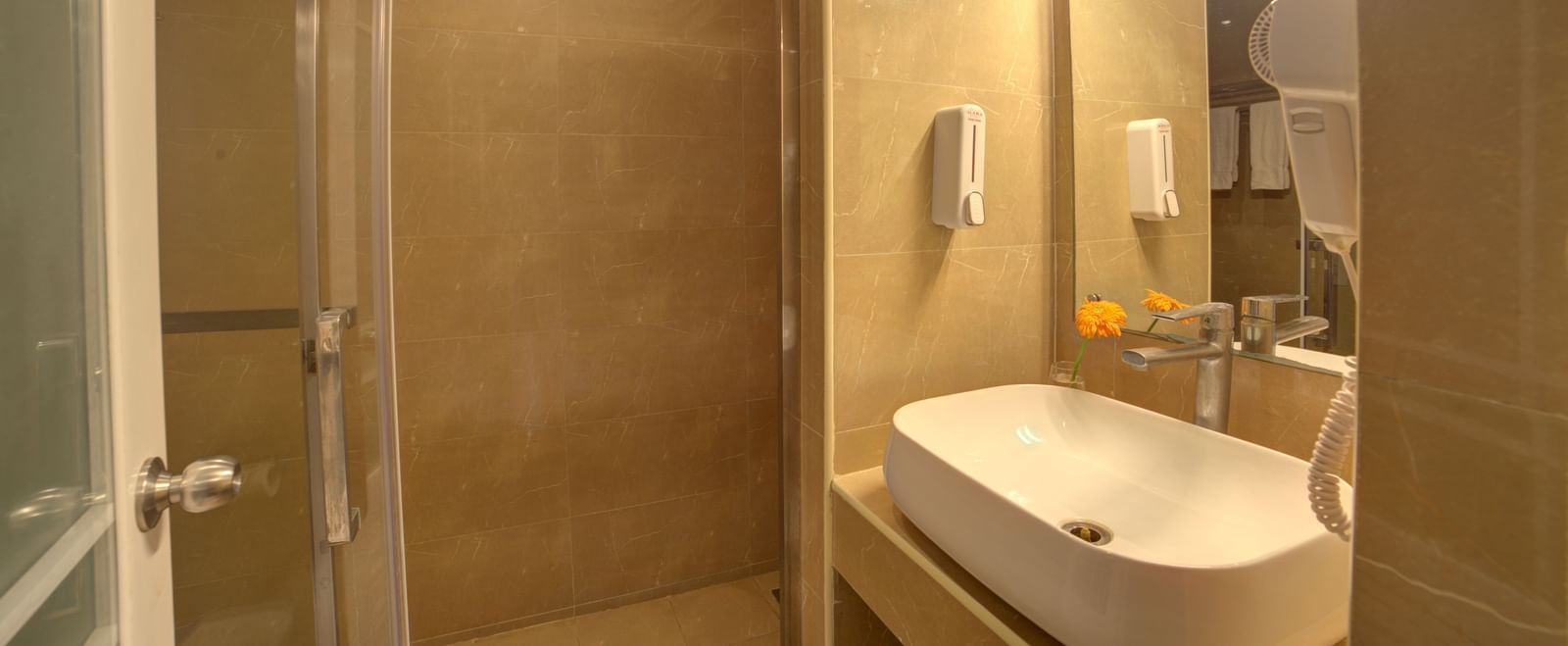 Modern bathroom with glass shower enclosure, large mirror, and wall-mounted amenities at Ilara Hotels & Spa, OMR, Chennai