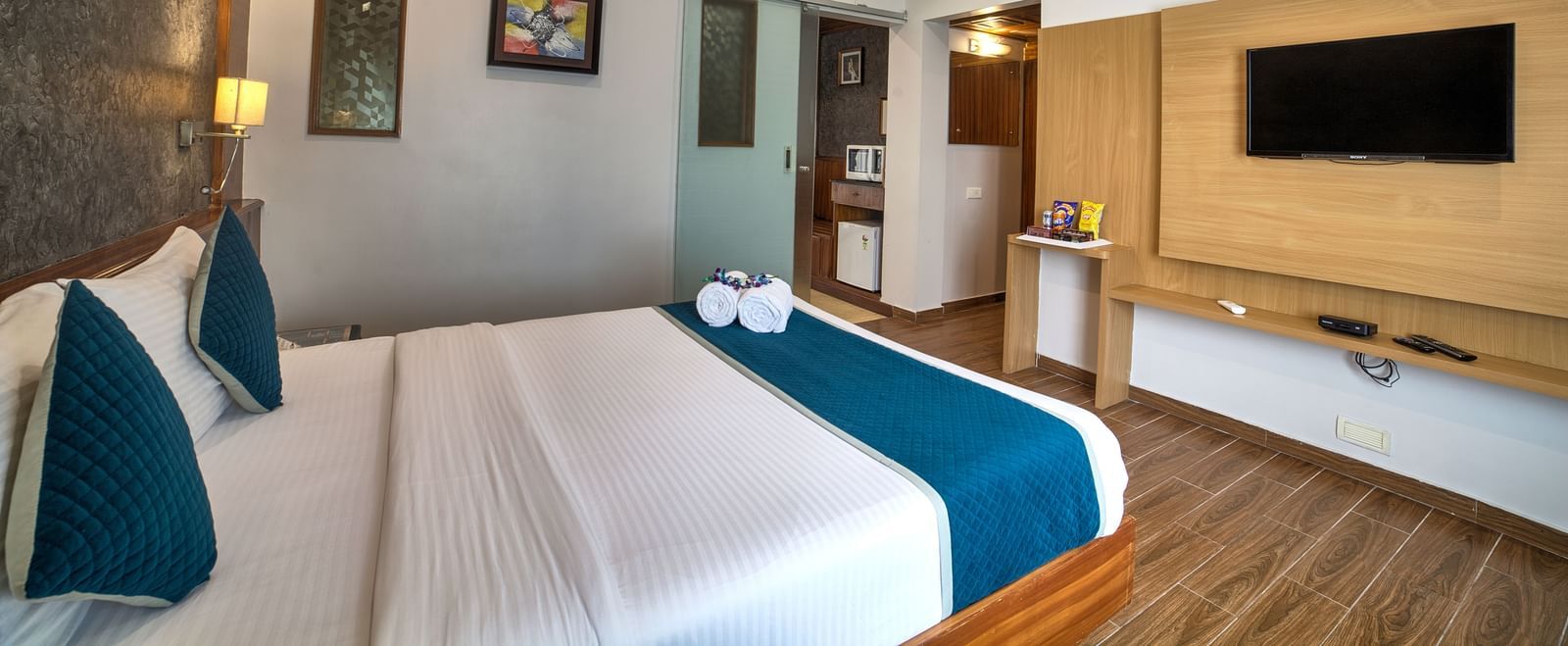 Modern bedroom with wooden flooring, soft lighting, and wall-mounted television at Ilara Hotels & Spa, OMR, Chennai