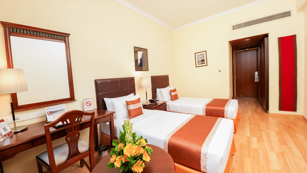 A room with twin beds, spreads, pillows, chairs, and a door. | MGM Mark Whitefield