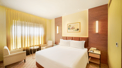 A warm-toned hotel room featuring a large bed, a desk area, and artwork on the walls | Suite | Sarovar Portico, Sriperumbudur