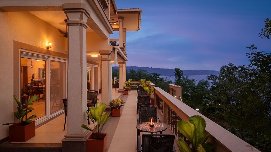 An outdoor dining area in Sindhudurg overlooking lush green trees and an ocean - Highland Sarovar Portico, Sindhudurg
