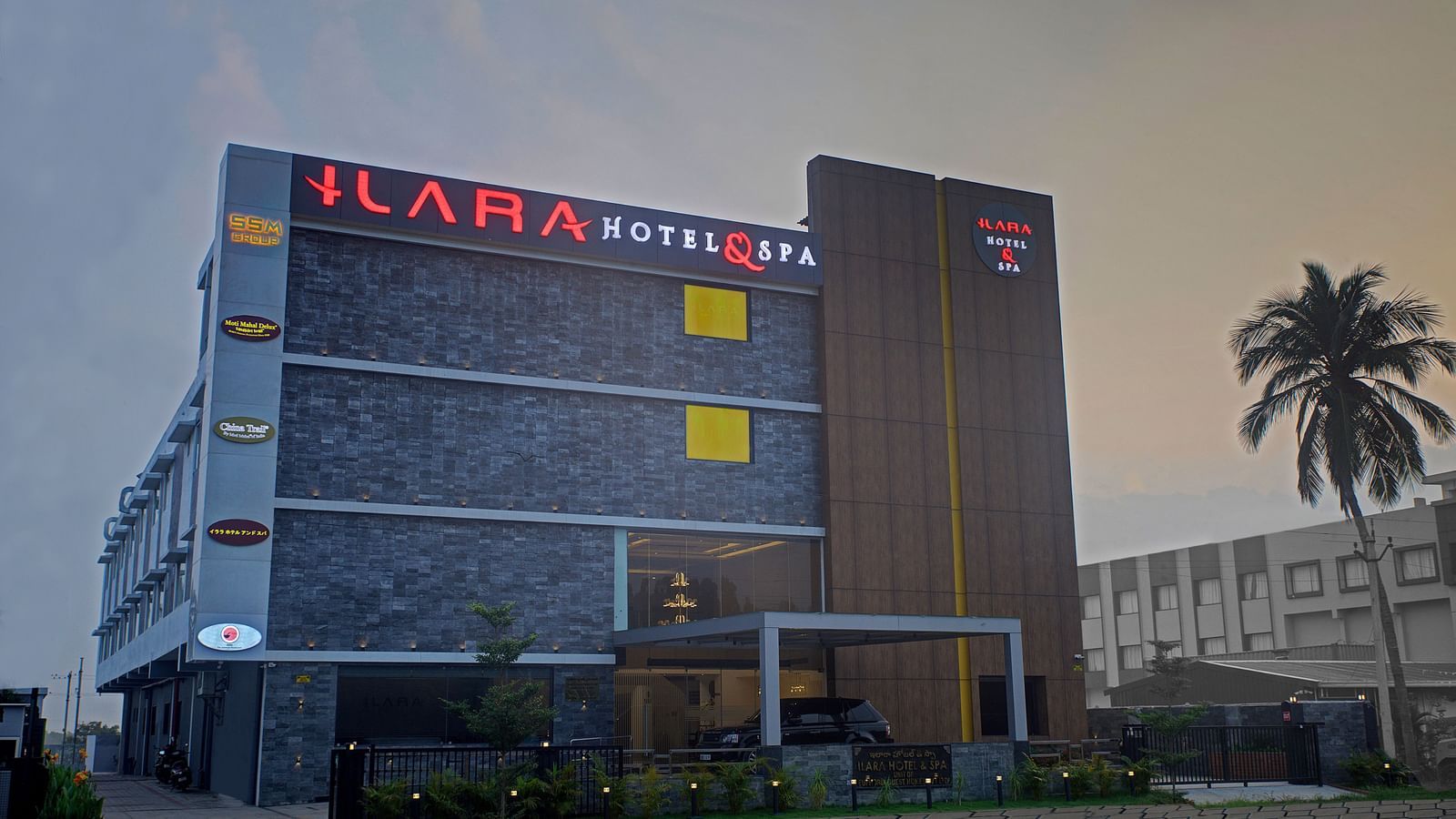 Exterior view of a contemporary hotel building with the hotel logo and a palm tree in the foreground at Ilara Hotels & Spa.