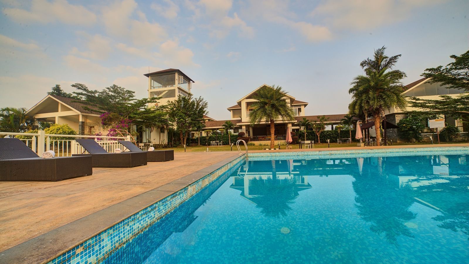 A serene outdoor swimming pool surrounded by palm trees and luxury villas under a bright blue sky at Ilara Hotels & Spa.