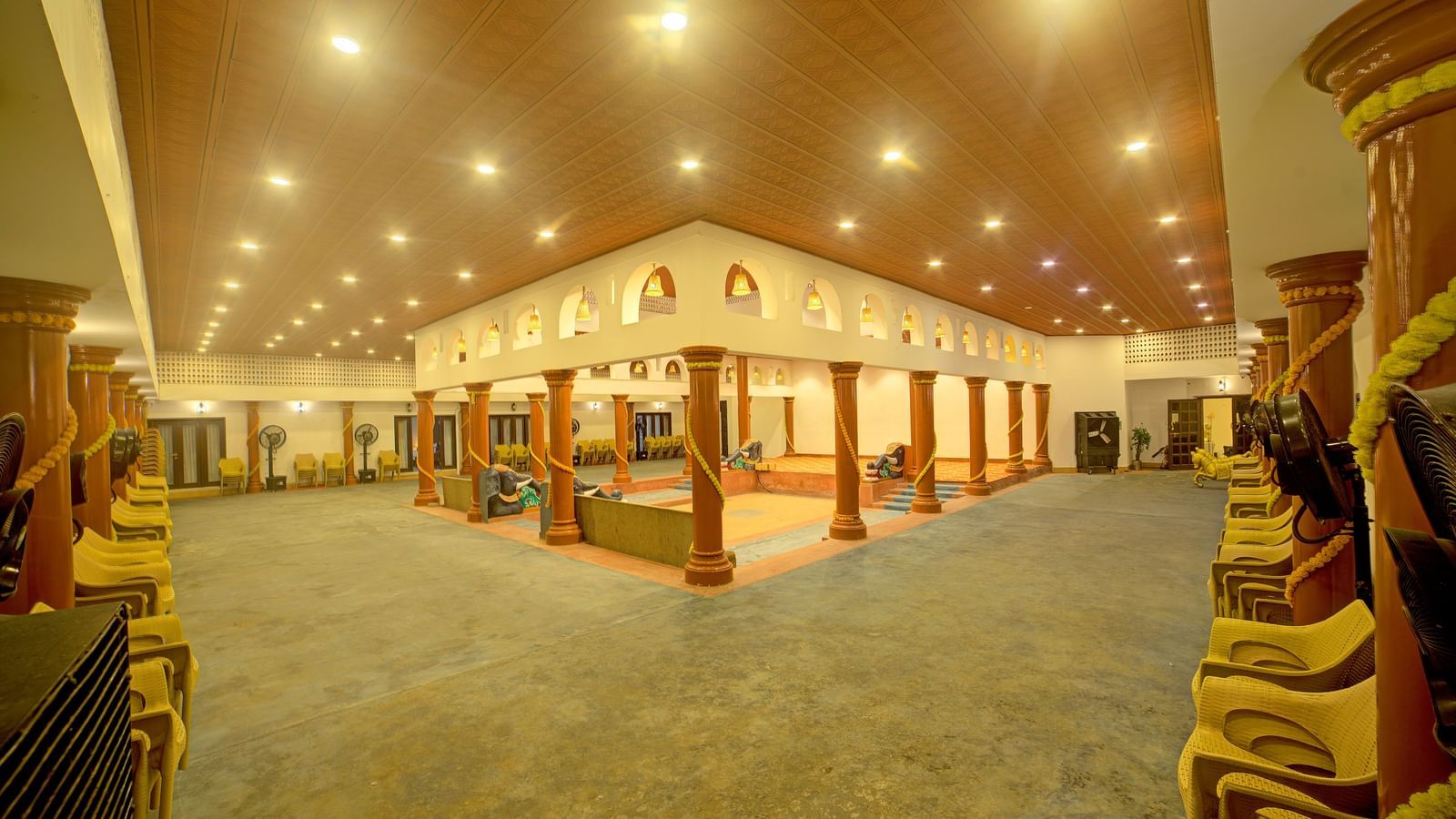 Illuminated traditional event hall with arched architecture and wooden seating at Kailash Conventions ECR.