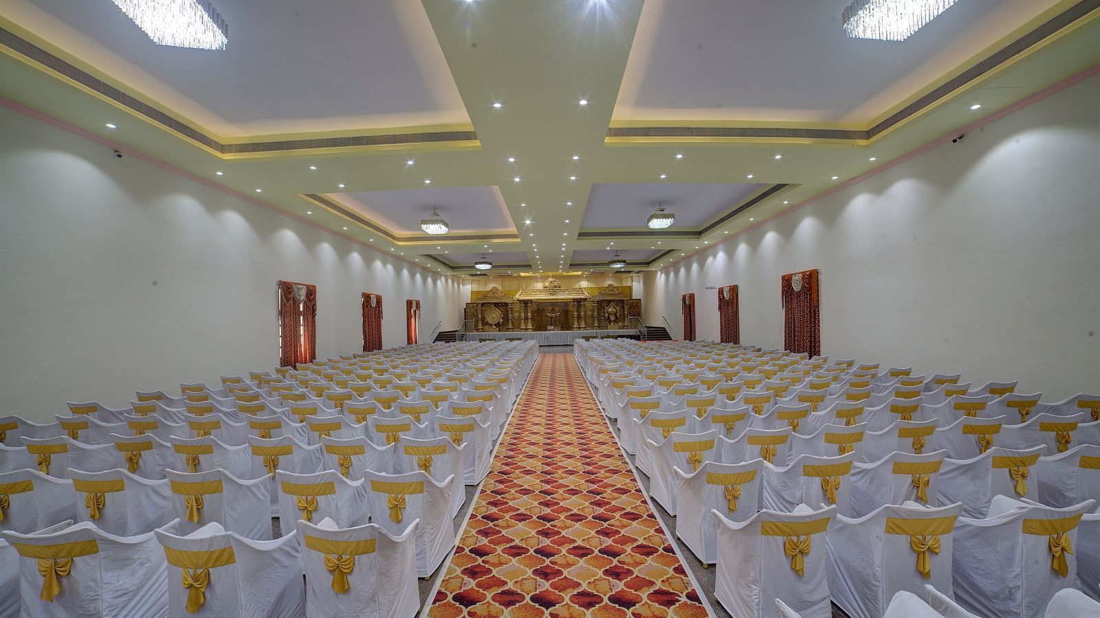 Indoor banquet hall with rows of white chairs and a central aisle at Kailash Conventions ECR.