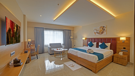 A brightly lit bedroom at the Junior Suite at Ilara Hotels & Spa, Tada with a double bed along with a bed side tables besides it.