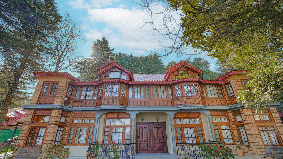 The facade of BluSalzz Terrah Hills Resort, Dalhousie, with a red roof, balconies, windows, and a landscaped area with benches in front.