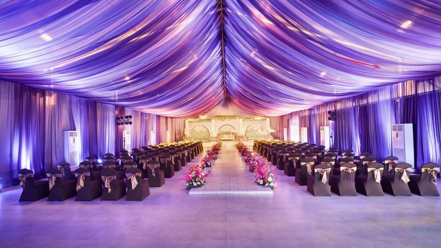 Elegant banquet hall with decorated roof in purple colour and rows of black covered chairs with flower centrepieces along the isle at Grande Bay Resort & Spa.