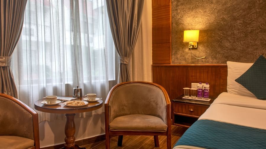 Cosy in-room seating with a round table and cushioned chairs by the window at Ilara Hotels & Spa, OMR, Chennai