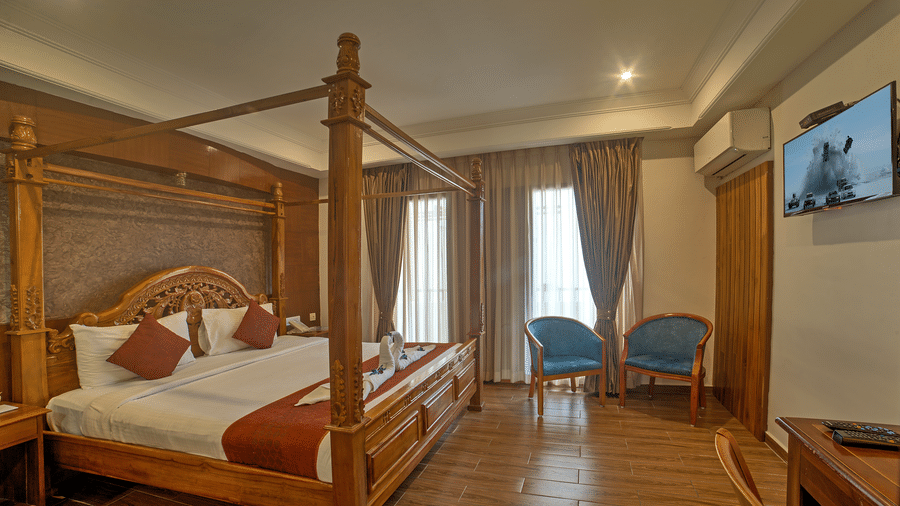 Elegant wooden bed with twin chairs and ambient lighting in a spacious room at Ilara Hotels & Spa, OMR, Chennai