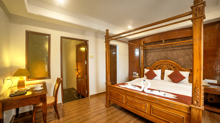 Luxurious four-poster bed with classic wooden furniture and warm ambient lighting at Ilara Hotels & Spa, OMR, Chennai