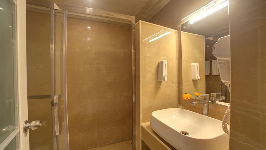 Modern bathroom with glass shower enclosure, large mirror, and wall-mounted amenities at Ilara Hotels & Spa, OMR, Chennai