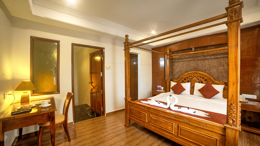 Luxurious four-poster bed with classic wooden furniture and warm ambient lighting at Ilara Hotels & Spa, OMR, Chennai
