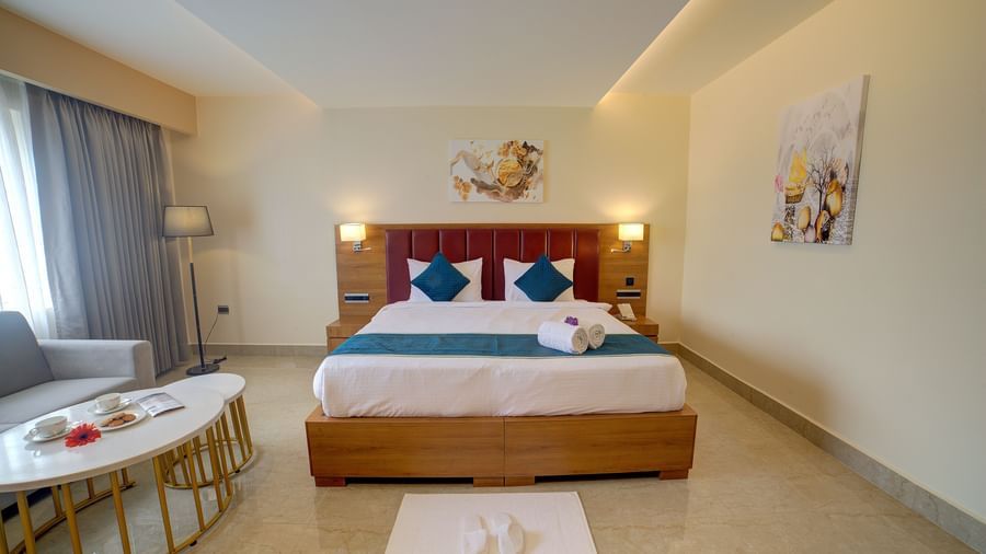 Front view shot of a comfortable double bed in the junior Suite with a common seating area besides it at Ilara Hotels & Spa, Tada.