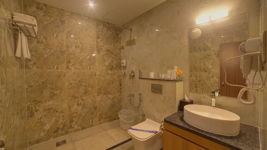 A warmly lit bathroom of the Junior Suite with a shower area along side a commode and a wash basin at Ilara Hotels & Spa, Tada.