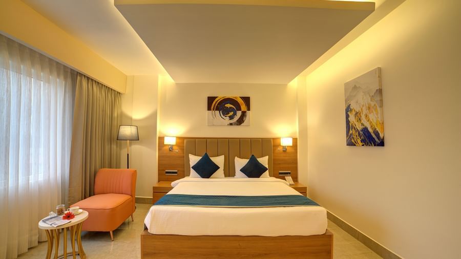 Front view shot of the double bed at the Signature Suite at Ilara Hotels & Spa, Tada with an orange cushioned chair and a small coffee table in front of it.