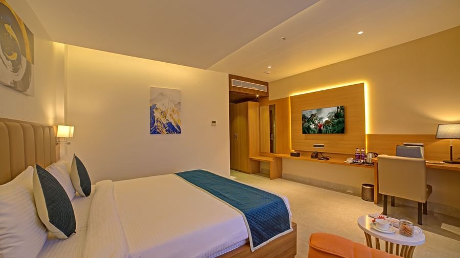 A wall mounted television in front of a comfortable double bed in front of it at in a warmly lit Signature Suite at Ilara Hotels & Spa, Tada.