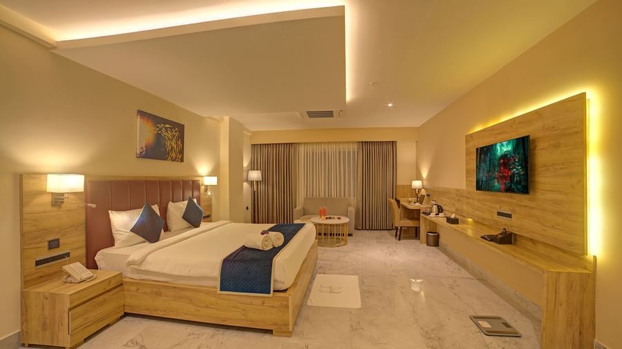 A warmly lit bedroom of the Junior Suite at Ilara Hotels & Spa, Tada featuring a double bed and wall mounted television in front of it.