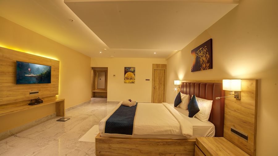 Side view shot of a double bed along in a warmly lit Junior Suite at Ilara Hotels & Spa, Tada with a false ceiling in the above it.