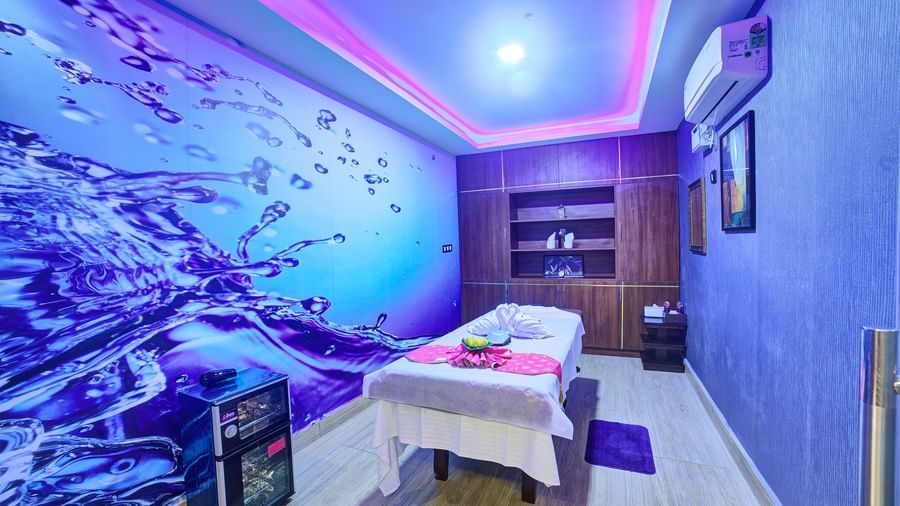 Corner view of a room with a spa table in the middle of the room with blue ambient light and a beautiful wallpaper in one of the walls at Ilara Hotels & Spa, Tada.