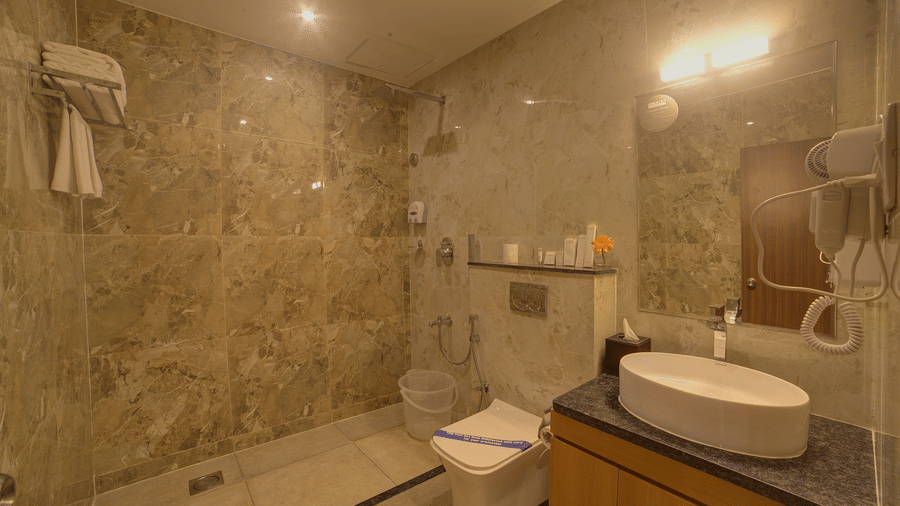 A warmly lit bathroom of the Junior Suite with a shower area along side a commode and a wash basin at Ilara Hotels & Spa, Tada.