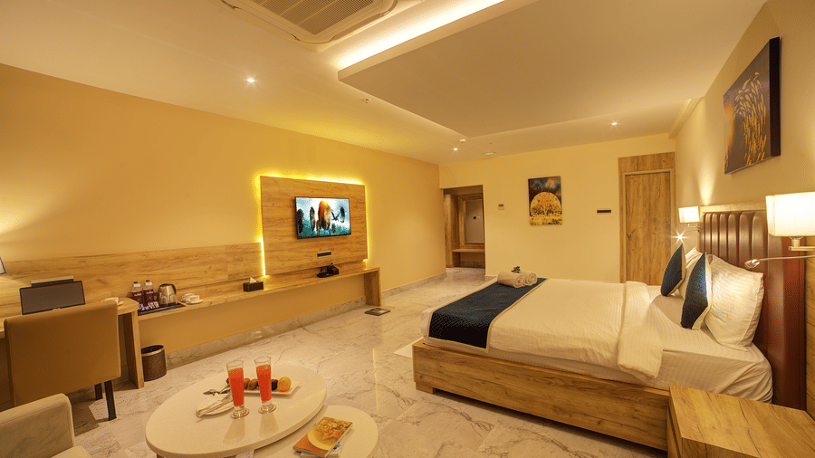 A wide-angle shot of the Junior Suite with a coffee table along with a double bed and a wall mounted television and a work station.