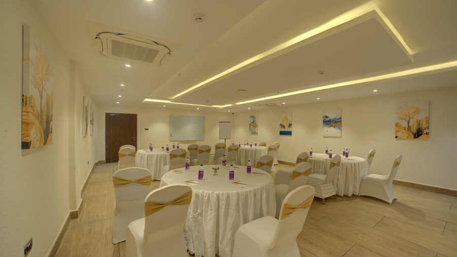 A spacious well-lit banquet hall with a back lit false ceiling with chairs and tables arranged for an event at Ilara Hotels & Spa, Tada.