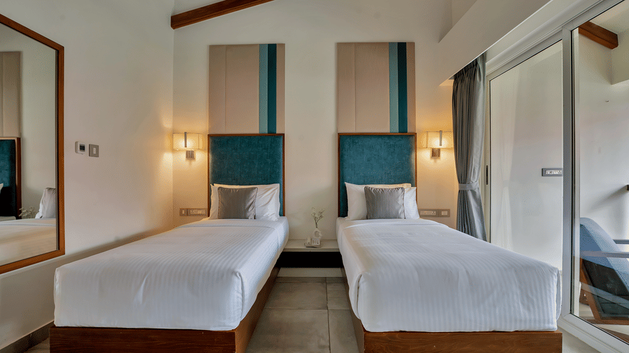 Twin Room at Mango Hill, Velankanni with 2 single beds, headboards, lamps, and a glass door leading to a balcony.