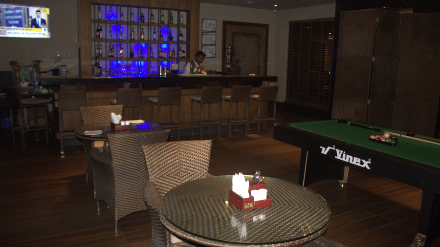 A table and a chair in a bar with a bartender and billiards table at the background at Pipul Padmaja Premium Hotel & Convention.